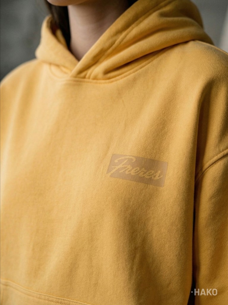 Detalle del logo frontal “Frères” estampado al tono sobre el buzo butter yellow.